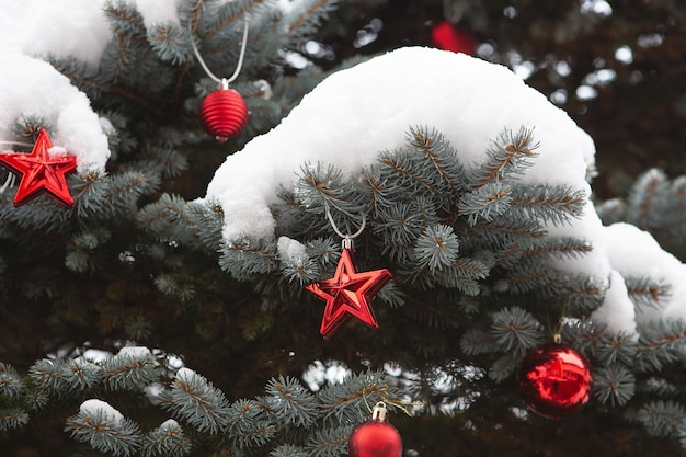 Zdjęcie zbliżenie sosny na świeżym powietrzu drzewo bożonarodzeniowe na świeżym powietrzu drzewo bożonarodzeniowe pokryte śniegiem i ozdobione czerwonymi kulami i gwiazdami