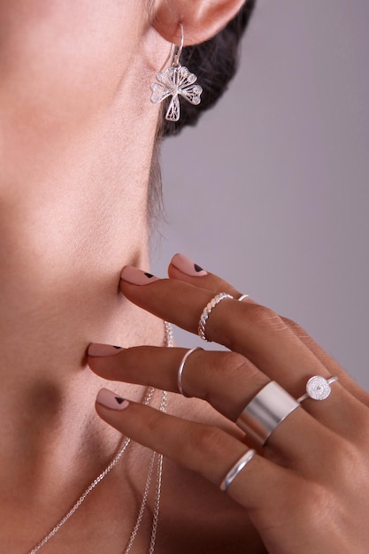 zbliżenie srebrnego kolczyka w kształcie filigranowej koniczyny i dłoni ze srebrnymi pierścionkami dotykającymi