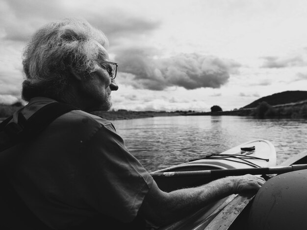 Zdjęcie zbliżenie starszego mężczyzny jeżdżącego kajakiem w jeziorze na tle nieba