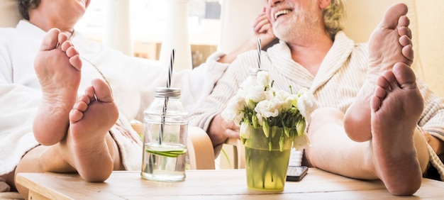 Zbliżenie stóp para seniorów na bajce w hotelu lub w domu przy koktajlu lub drinku - zdrowy i wspaniały styl życia - ciesząc się razem siedząc w domu