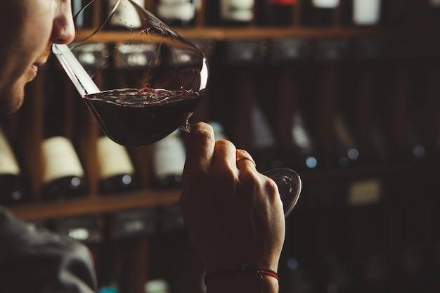 Zdjęcie zbliżenie strzał młodego sommeliera zapach czerwonego wina na tle piwnicy z winami