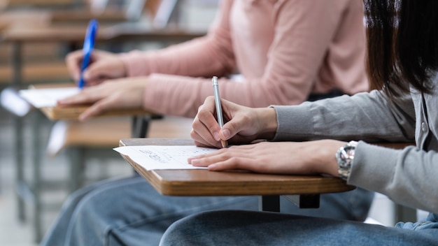 Zbliżenie studentów piszących notatkę na zeszycie w klasie podczas słuchania i studiowania wykładu. Zbliżenie na kobiece dłonie piszące na notatniku umieszczonym na drewnianym pulpicie