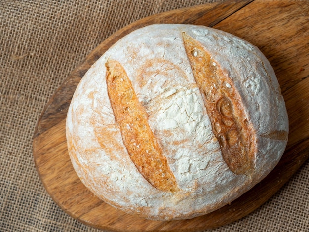 Zbliżenie świeżego chrupiącego chleba pszennego o okrągłym kształcie na tle lnu drewniana deska do krojenia Widok z góry płaskiej pozycji
