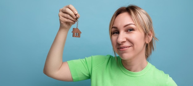 Zdjęcie zbliżenie szczęśliwej ślicznej blond kobiety w swobodnym wyglądzie trzymającej pęku kluczy do mieszkania na niebieskim tle