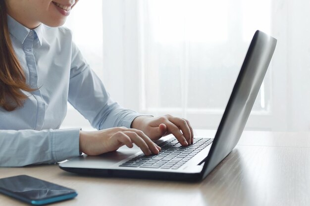 Zbliżenie szczęśliwej uśmiechniętej kobiety pracującej na laptopie, siedzącej przy stole przy oknie