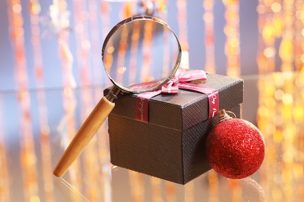 Zbliżenie szkła powiększającego i pudełka na prezenty z ozdobami świątecznymi w tle