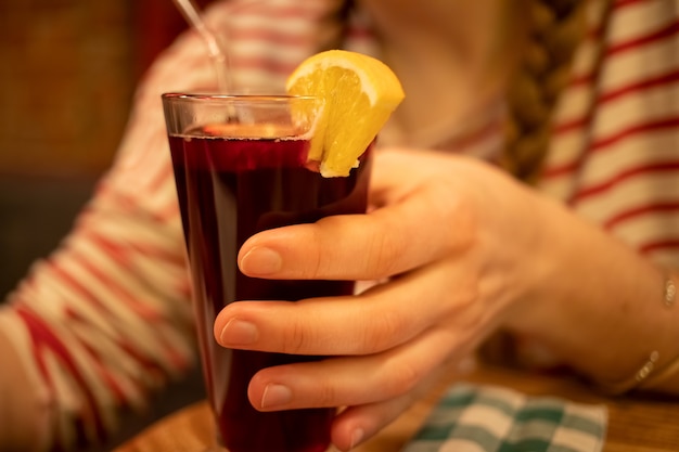 Zbliżenie Szklanego Kubka Z Pysznym Aromatycznym Domowym Grzanym Winem Z Cytrynowym Wystrojem Trzymanym Przez Dziewczynę W Rozmyciu. Nieostrość,