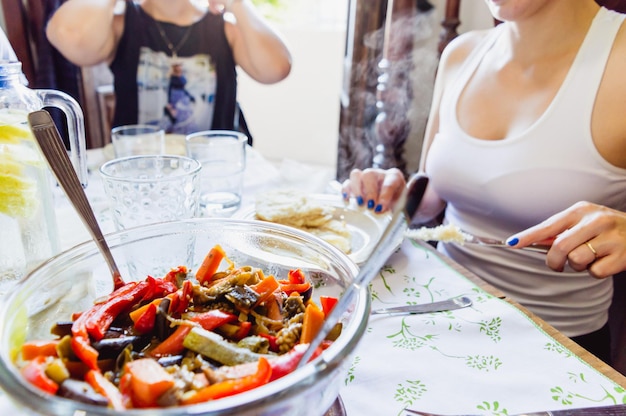 Zbliżenie szklanej miski z smażonymi warzywami na stole z zamazanymi ludźmi w tle