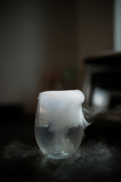 Zbliżenie szkło z białą mgłą przy ciemnym tłem. Reakcja chemiczna suchego lodu z wodą.