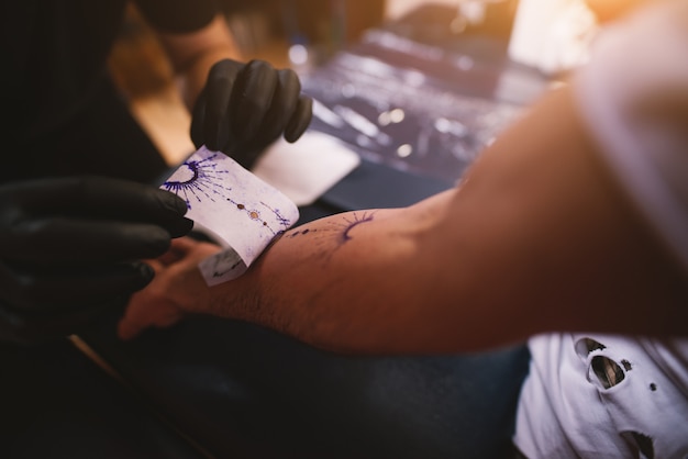 Zbliżenie tatuażystów usuwających naklejkę, którą wcześniej zrobił z ramienia klienta.