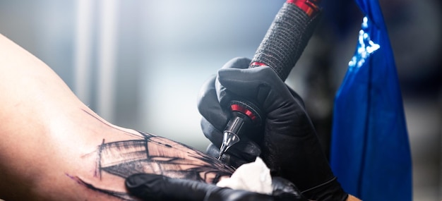 Zbliżenie tatuażysty tatuuje czarny tatuaż farbą tatuaż wypełnia proces tatuażu obwodu tatuażu