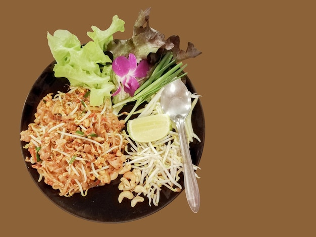 Zbliżenie tradycyjnego tajskiego jedzenia PadThai na czarnym kolorze płytki ceramicznej z płytą po stronie warzyw izolować na brązowym tle