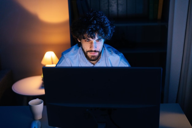 Zbliżenie twarzy skoncentrowanego brodatego mężczyzny uważnie patrzącego na ekran monitora podczas pracy na komputerze