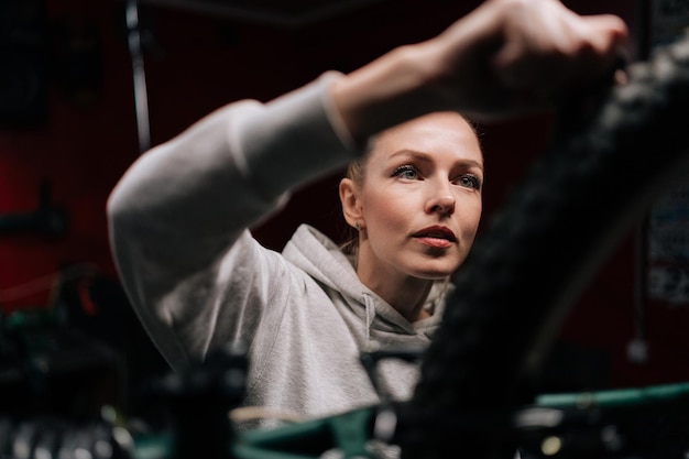 Zbliżenie twarzy skupionej fachowca naprawiającej i naprawiającej rower górski stojącej na stojaku rowerowym w warsztacie naprawczym z ciemnym wnętrzem