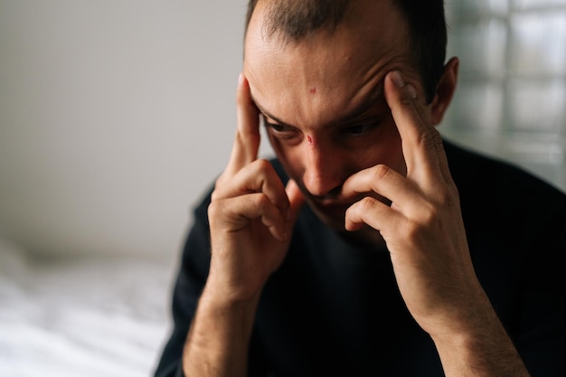 Zbliżenie twarzy wyczerpanego mężczyzny siedzącego samotnie w domu dotykającego głowy, który czuje się smutny, sfrustrowany, przygnębiony, cierpiący na ból głowy po kłótni z żoną