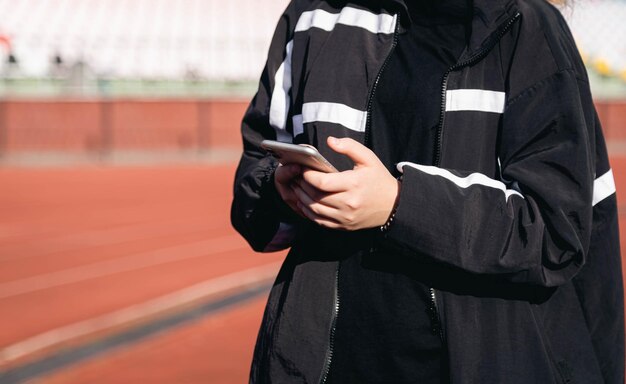 Zbliżenie uczennica za pomocą smartfona w koncepcji treningu na świeżym powietrzu stadionu sportowego