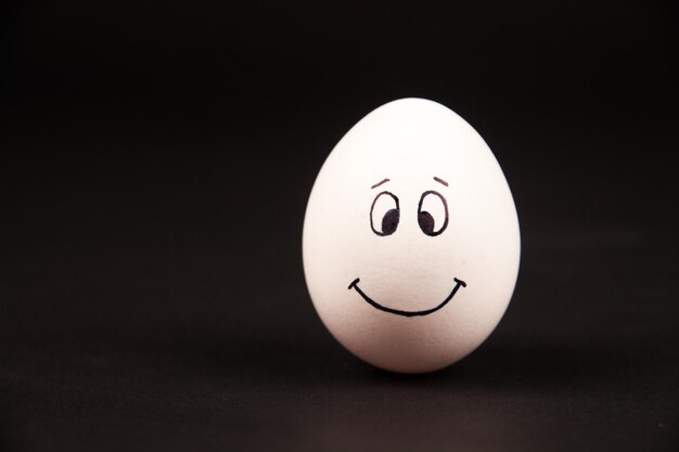 Zdjęcie zbliżenie uśmiechniętej twarzy na jajku na czarnym tle