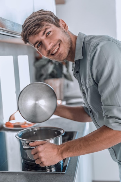 Zdjęcie zbliżenie uśmiechnięty mężczyzna zagląda do garnka z jedzeniem