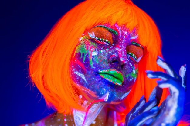 Zbliżenie UV portret modelki z artystycznym kolorowym makijażem i pomarańczową peruką z zamkniętymi