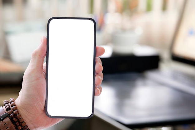 Zbliżenie widok człowieka ręki trzymającej pusty ekran smartphone z niewyraźne tło pokoju biurowego.