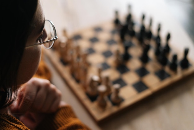 Zbliżenie widok z tyłu zamyślonej młodej kobiety w eleganckich okularach myślącej o szachowym ruchu siedzącej w ciemnym pokoju selektywnej ostrości