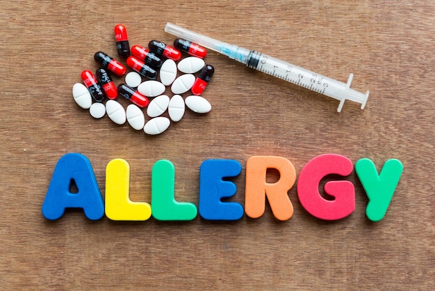 Zdjęcie zbliżenie wielokolorowego tekstu o alergii z pigułkami i strzykawką na stole