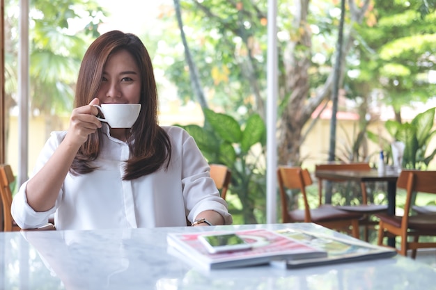 Zbliżenie wizerunek wącha kawę i pije gorącą kawę z czuć dobrze azjatykcia kobieta