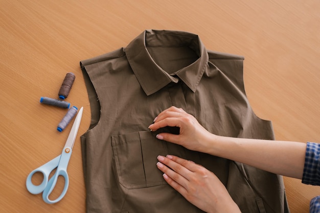 Zbliżenie z góry na ręce krawcowej młoda kobieta ręcznie pracuje nad projektem nowej kolekcji koszul khaki Na stole w pobliżu znajdują się nici i nożyczki