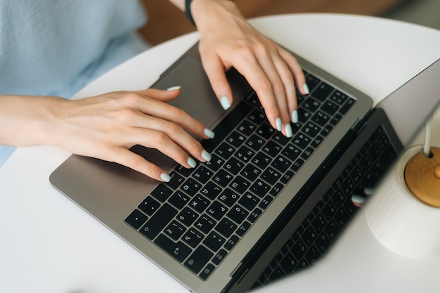 Zbliżenie z góry nierozpoznawalna młoda kobieta pisząca na klawiaturze laptopa, siedząca przy stole w kawiarni