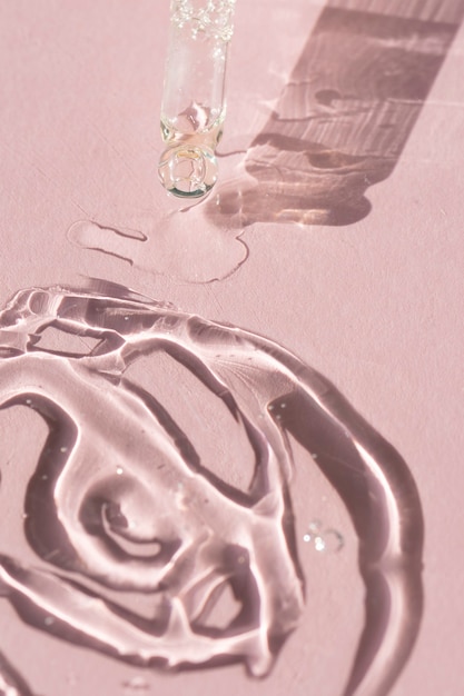 Zbliżenie zakraplacza z pipetą z wylewającym serum do twarzy na różowym tle do Twojego projektu kosmetycznego