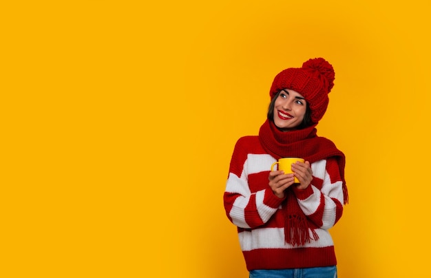 Zbliżenie zdjęcie uroczej, szczęśliwej, stylowej, delikatnej kobiety w czerwonych zimowych ubraniach trzyma napój w żółtej filiżance w dłoniach i relaksuje