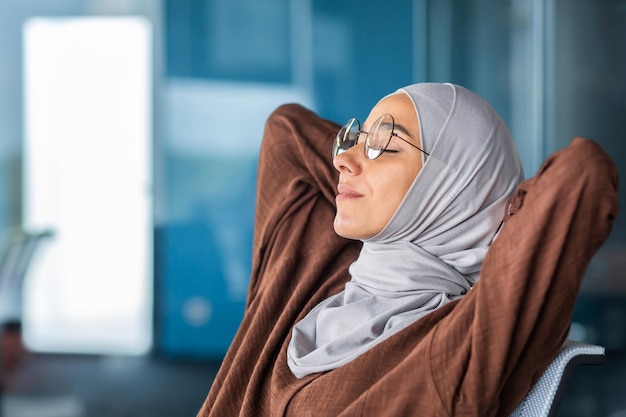 Zbliżenie zdjęcie z boku zmęczona młoda arabska kobieta w hidżabie i szkłach siedzi w biurze na