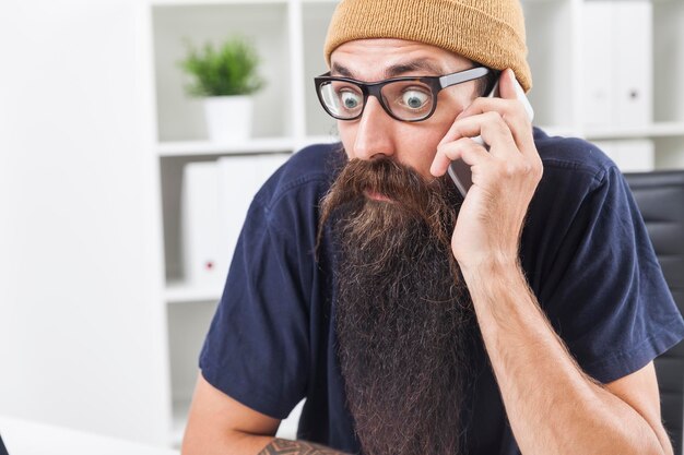 Zdjęcie zbliżenie zdumionego mężczyzny z długą brodą na telefonie