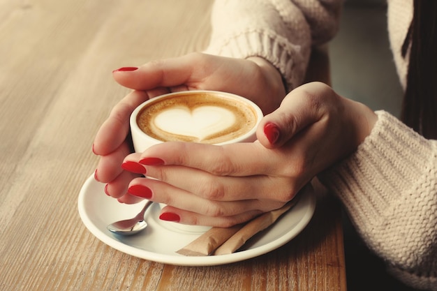 Zbliżenie żeńskie ręki z czerwonym żelowym manicure'em trzyma filiżankę z kawą