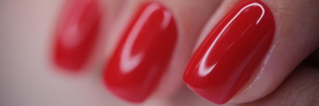 Zbliżenie żeńskiej dłoni z czerwonym, jasnym, błyszczącym lakierem, idealnym manicure, paznokci, salonem piękności i