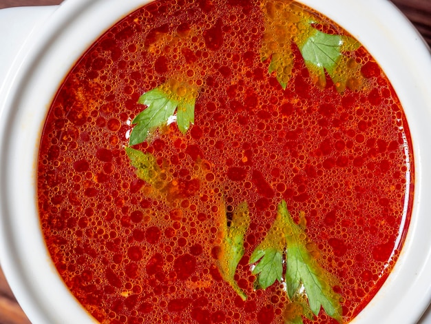 Zdjęcie zbliżenie: zupa barszcz w białej ceramicznej misce zupy. tradycyjna zupa dla rosji i ukrainy. na zupie unoszą się warzywa. widok z góry, układ płaski