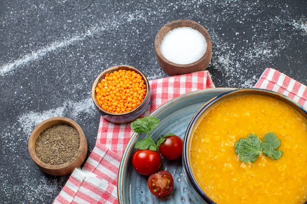 Zbliżenie zupy z czerwonej soczewicy w misce podawanej z solą z zielonych pomidorów i pieprzu na niebieskiej tacy na czerwonym ręczniku w paski i różnych przyprawach na czarno białym tle