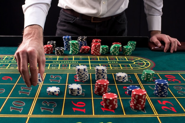 Zbliżenie żywy obraz zielonego stołu kasyna z ruletką, z rękami krupiera i wielokolorowe żetony.