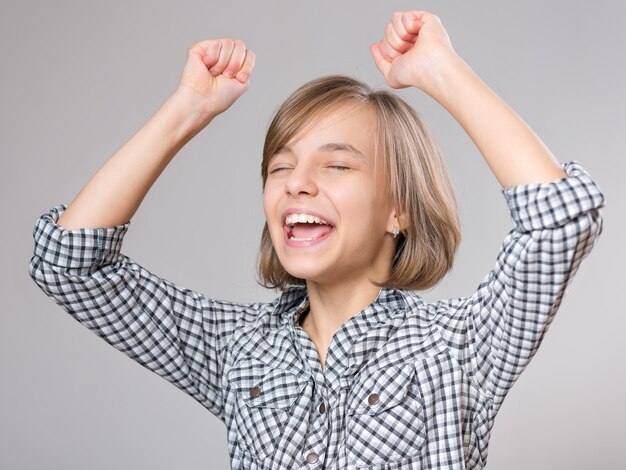 Zdjęcie zbliżony emocjonalny portret białej dziewczynki zabawny krzyczący o zwycięstwie nastolatek na szarym tle szczęśliwa uczennica świętująca triumf krzycząc z rękami w górze