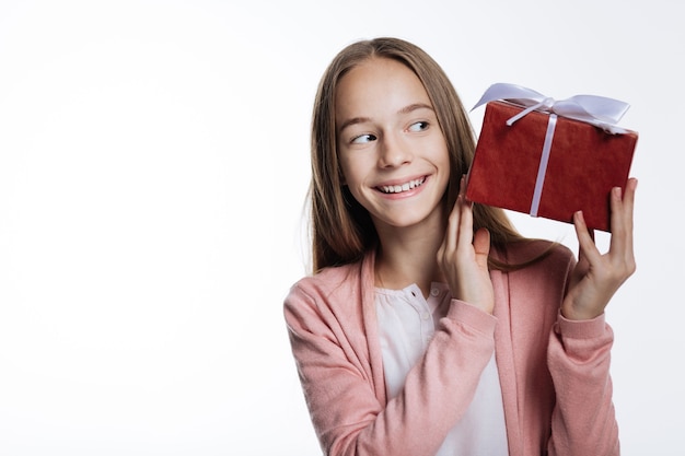 Zbyt ciekawy. Przyjemna radosna nastolatka podnosi pudełko z prezentem i zerka na nie z ciekawością, chcąc poznać jego zawartość