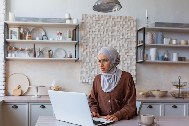 Zdalna muzułmańska młoda kobieta w hidżabie freelancer pracująca z domu online na laptopie siedzącym w