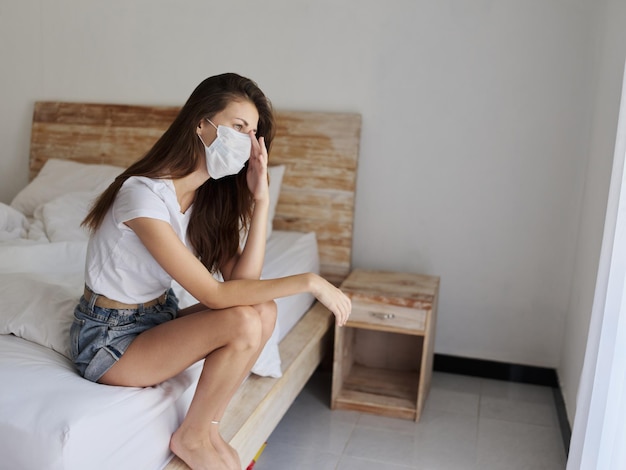 Zdenerwowana kobieta nosząca maskę medyczną siedząca na łóżku w hotelu, wakacje, kwarantanna, izolacja, zdjęcie wysokiej jakości