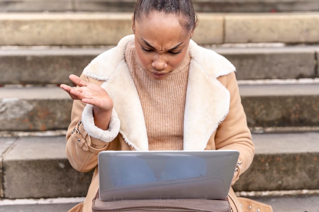 Zdenerwowana kobieta, studentka, ucząca się kursu padającego, pracująca na schodach, oglądająca seminarium internetowe za pomocą laptopa