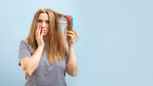 Zdjęcie zdenerwowana młoda kobieta patrząca z szokiem na swoje uszkodzone włosy na niebieskim tle