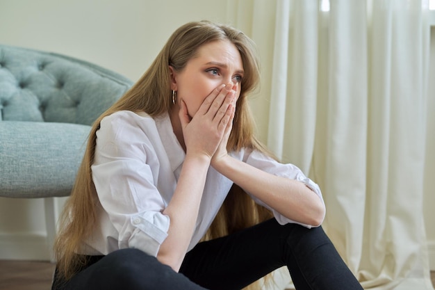 Zdenerwowana płacząca młoda kobieta siedzi w domu na podłodze