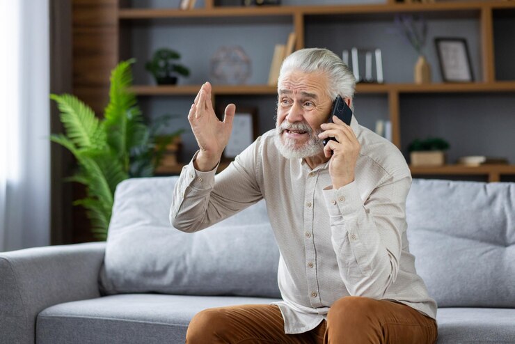 Zdjęcie zdenerwowany i wściekły starszy mężczyzna rozmawiający przez telefon w domu siedzący na kanapie i wyrazisty