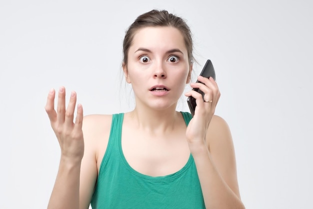 Zdjęcie zdezorientowana kobieta z telefonem komórkowym na szarym tle