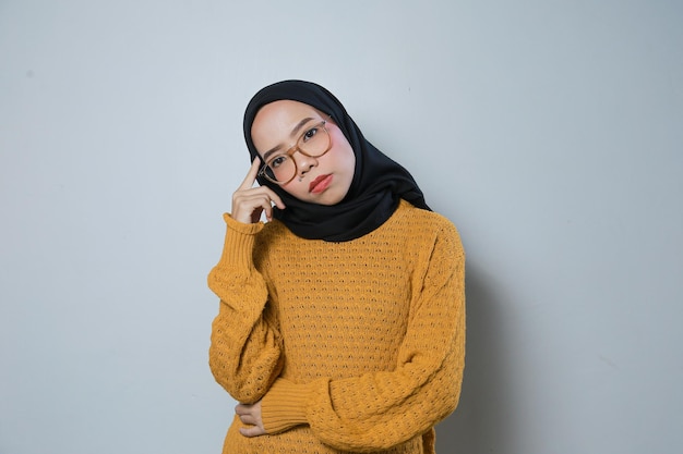 Zdezorientowana piękna młoda azjatycka muzułmańska biznesmenka w pomarańczowym swetrze i okularach myśląca