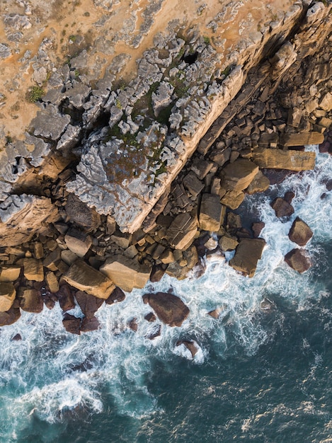 Zdjęcia lotnicze zrujnowanej chropowatej ściany z kawałkami skały spadły na falistym wybrzeżu w Peniche, Portugalia