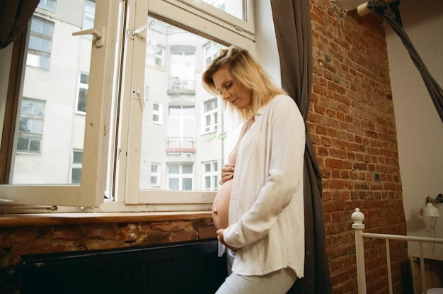 Zdjęcie analogowe przy oknie zdrowa piękna kaukaska młoda kobieta w ciąży stojąca obok